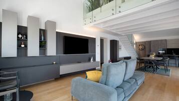 Un soggiorno moderno con un divano grigio, una televisione a schermo piatto e un'area pranzo con tavolo e sedie.