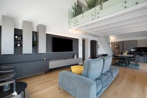 A modern living room with a grey sofa, a flat-screen TV, and a dining area with a table and chairs. - 'Luxury Terrazza' Apartment with Sea View, Wi-Fi, and Air Conditioning (Bari)