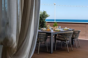 A table set outdoors with chairs, a view of the sea, and a curtain partially covering the window.