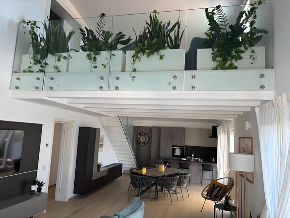 A modern loft apartment with a dining area, kitchen, and a balcony with plants.