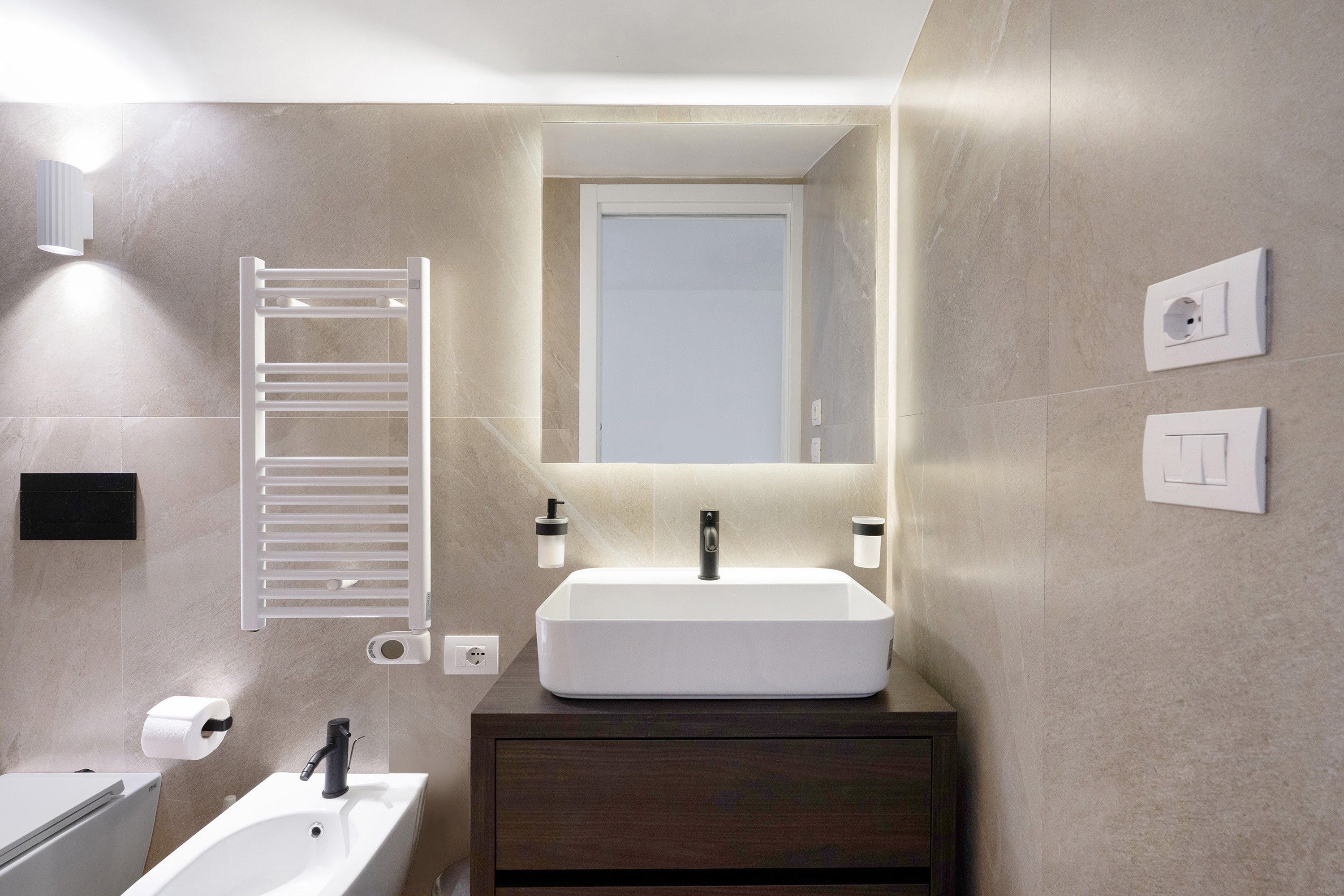 A modern bathroom with a white sink, dark wooden vanity, a towel rack, and a mirror.