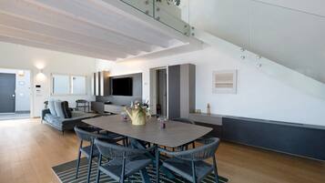 A modern interior with a dining area, a sofa, a TV, and a staircase.