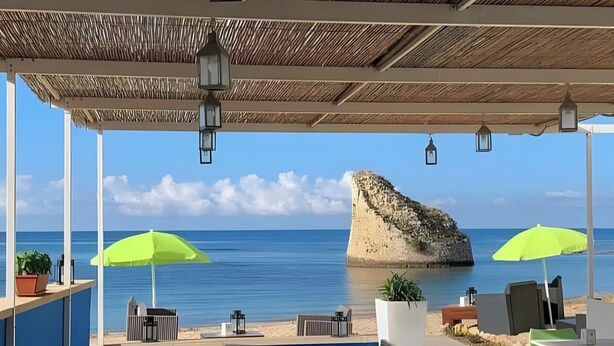 Zona junto a la piscina con mobiliario exterior, vista al mar y una formación rocosa.