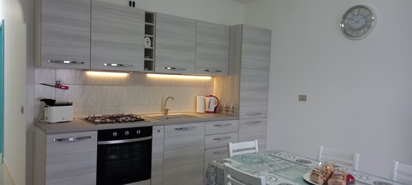 Una cocina moderna con estufa a gas, horno, pileta y una mesa de comedor con sillas.