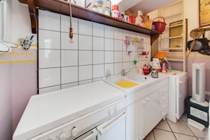 A kitchen with white cabinets, a sink, and a stove. There are shelves above the sink with various items.
