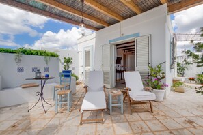 A covered outdoor seating area with white chairs and a table, a wooden ceiling, and potted plants.