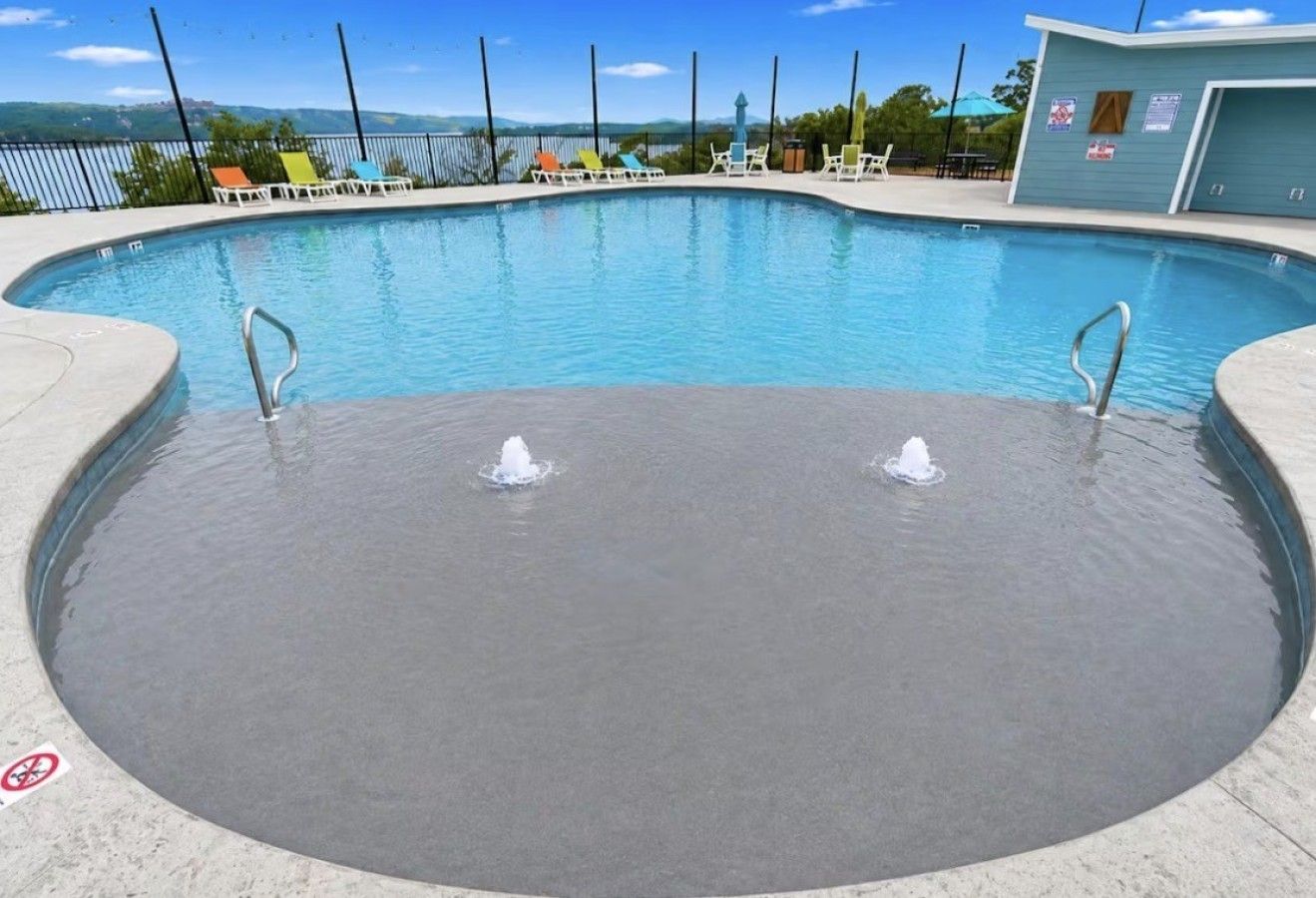 Una piscina con dos fuentes, rodeada de sillas de descanso y un edificio con señalización.