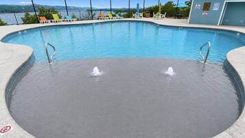 Una piscina con dos fuentes, rodeada de sillas de descanso y un edificio con señalización.