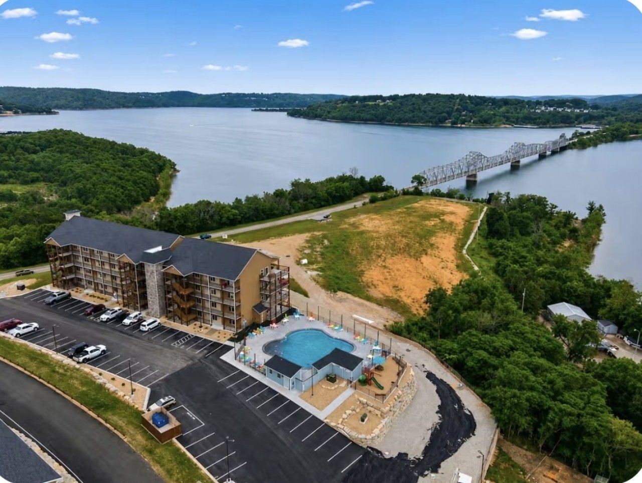 A hotel with a swimming pool, parking lot, and a view of a bridge over a lake.