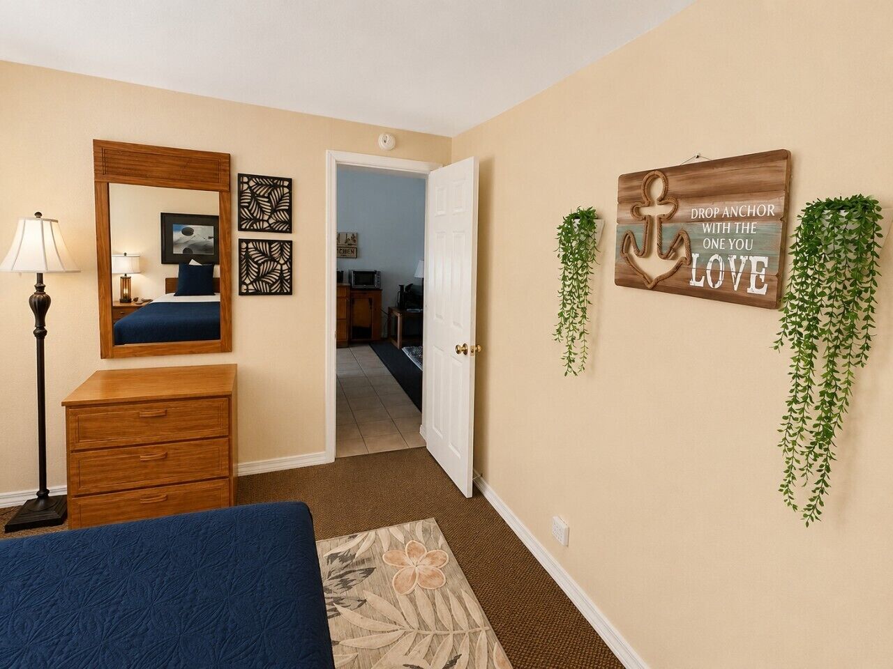 Een slaapkamer met een bed, een dressoir, een spiegel en wanddecoraties, waaronder een bord en planten.