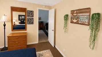 Een slaapkamer met een bed, een dressoir, een spiegel en wanddecoraties, waaronder een bord en planten.