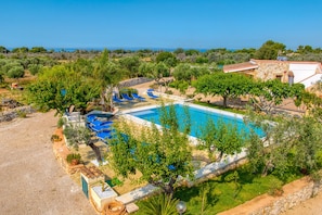 Ein Swimmingpool mit Liegestühlen, umgeben von Bäumen und einem Steinhaus.
