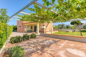 Ein Gebäude mit überdachter Terrasse, einem Garten und blauem Himmel.