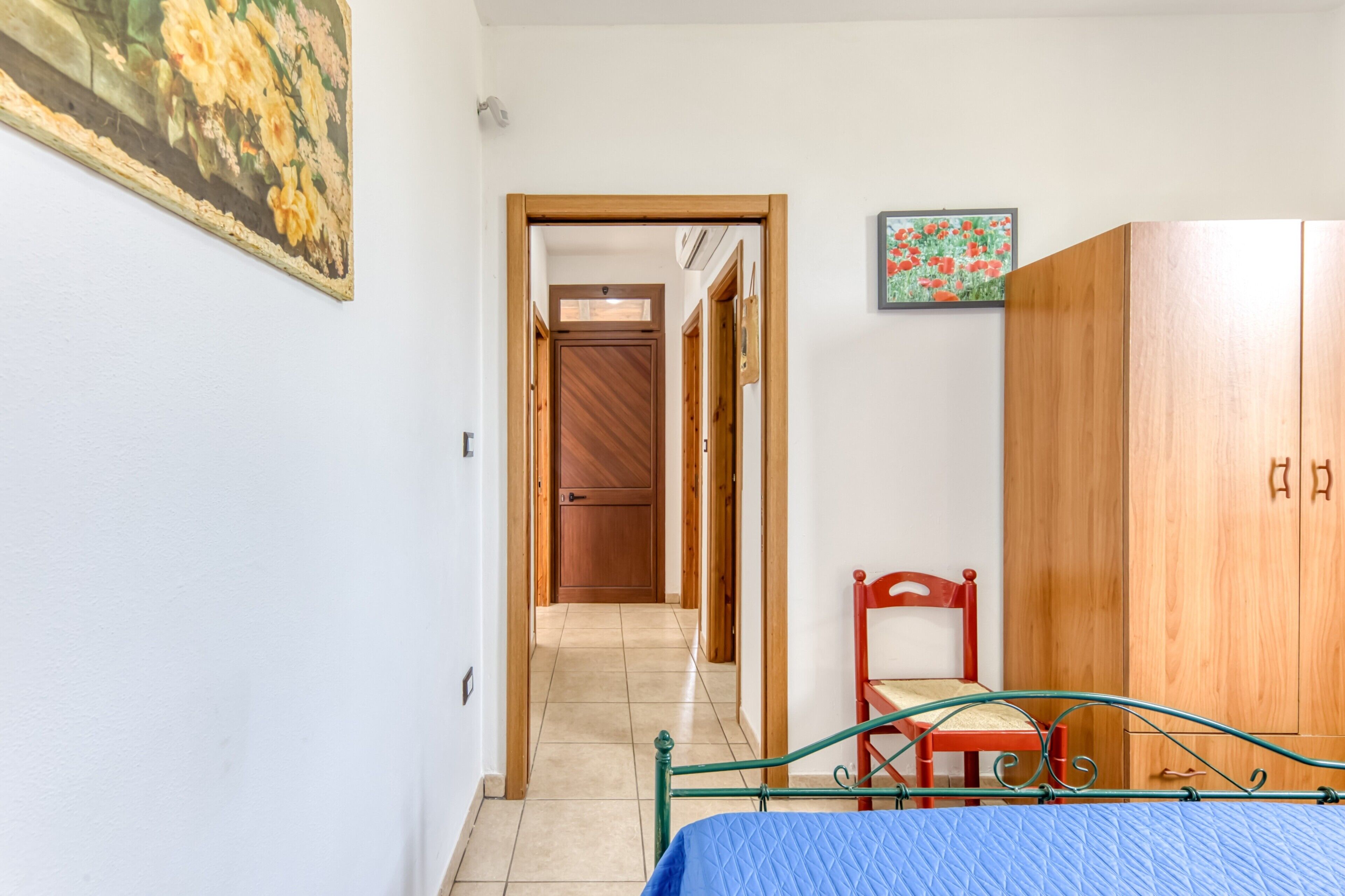 Une chambre à coucher avec un lit, une armoire en bois, une chaise rouge et un couloir menant à une porte.