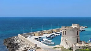 Una marina costera con una torre histórica, barcos y un litoral rocoso.