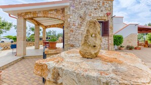 Un edificio de piedra con un patio cubierto, mobiliario exterior y una gran roca como centro de atención.