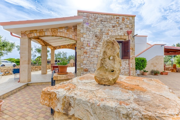 Un bâtiment en pierre doté d’un patio couvert, d’un espace extérieur aménagé pour s’asseoir et d’un grand rocher servant d’élément central.