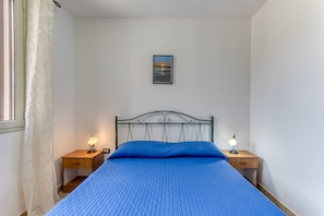 Une chambre à coucher avec un lit, deux tables de chevet avec des lampes, un tableau encadré au mur et une fenêtre avec des rideaux.