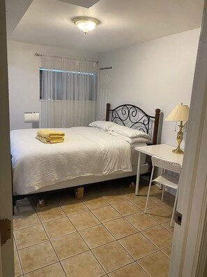 Une chambre à coucher avec un lit, une table de chevet, une lampe et une fenêtre avec des rideaux.