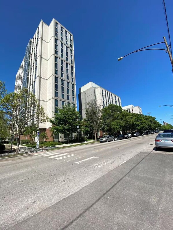 Un immeuble à plusieurs étages doté d’une architecture moderne, un ciel dégagé et une rue bordée de voitures garées.