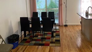 Een kamer met een eettafel en stoelen, een blauwe prullenbak, een vloerlamp en uitzicht op een balkon met een kerstboom.