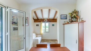 A dining area with a wooden table, chairs, a glass door, a white sofa, and a window with a view. - Holiday Home 'Villetta Cosimo' with Shared Pool, Private Garden and Air Conditioning (Morciano di Leuca)