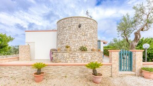 A stone cylindrical structure with a door, surrounded by potted plants and a gravel path. - Holiday Home 'Villetta Cosimo' with Shared Pool, Private Garden and Air Conditioning (Morciano di Leuca)