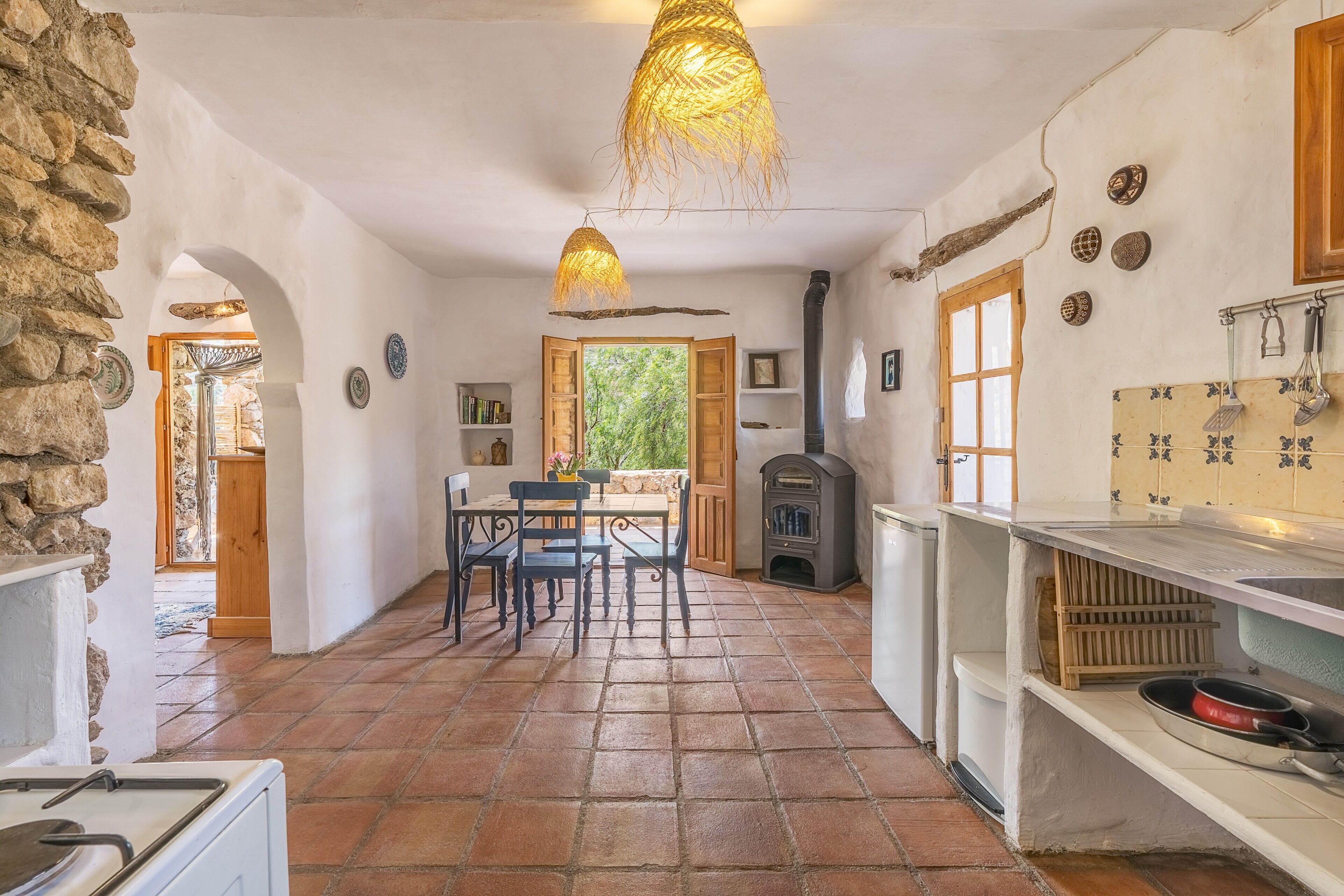 Cocina rústica con pared de piedra, zona de comedor con mesa y sillas, y vista a través de una puerta abierta.