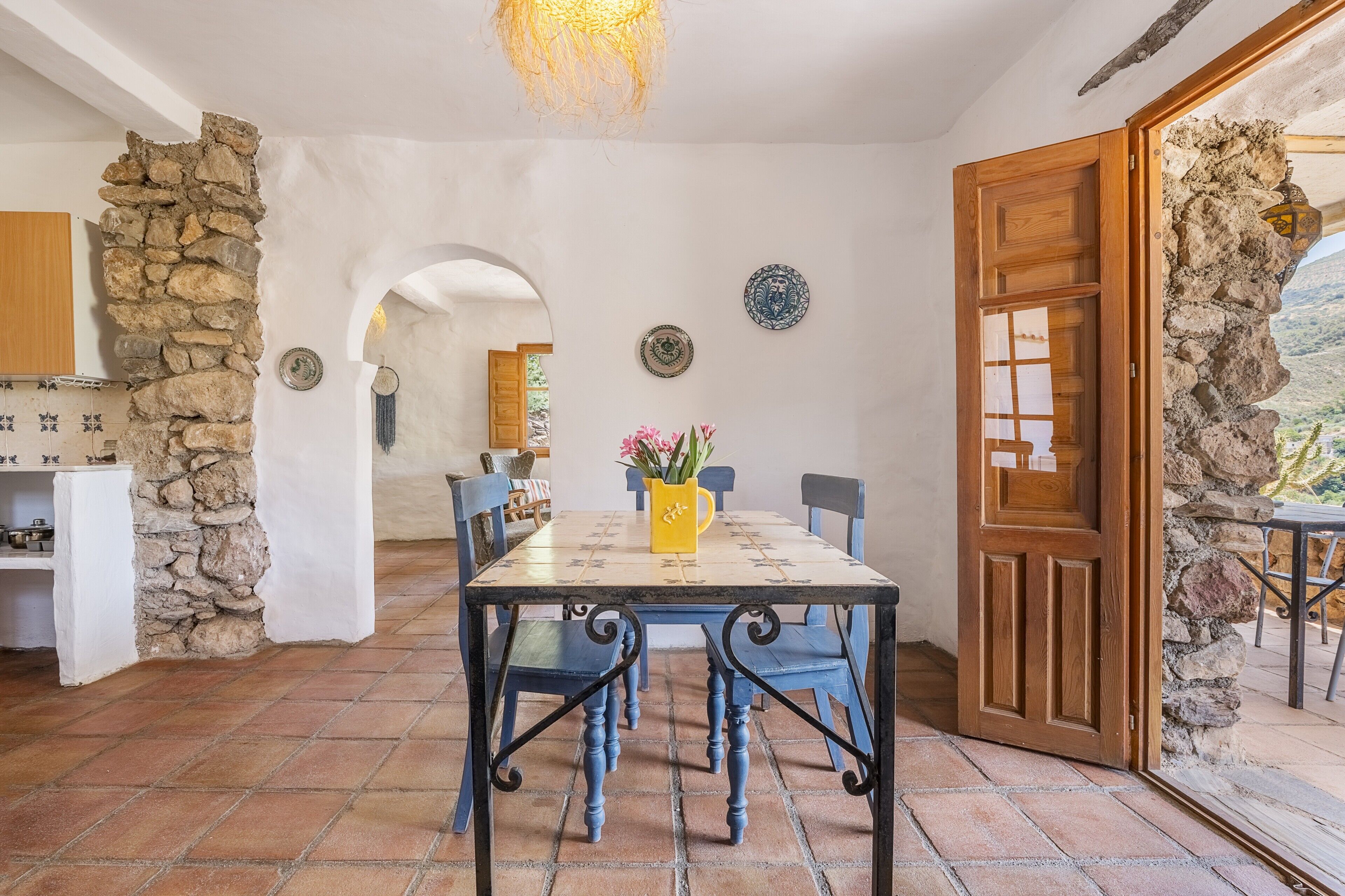 A dining area with a stone wall, a wooden door, and a view through an archway.
