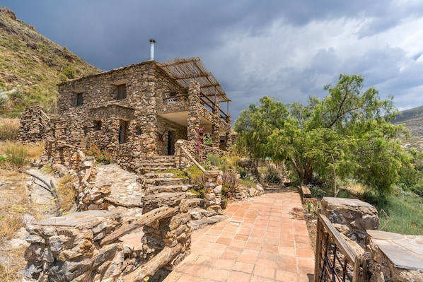 A stone building with a thatched roof, a staircase leading to the entrance, and a paved pathway.
