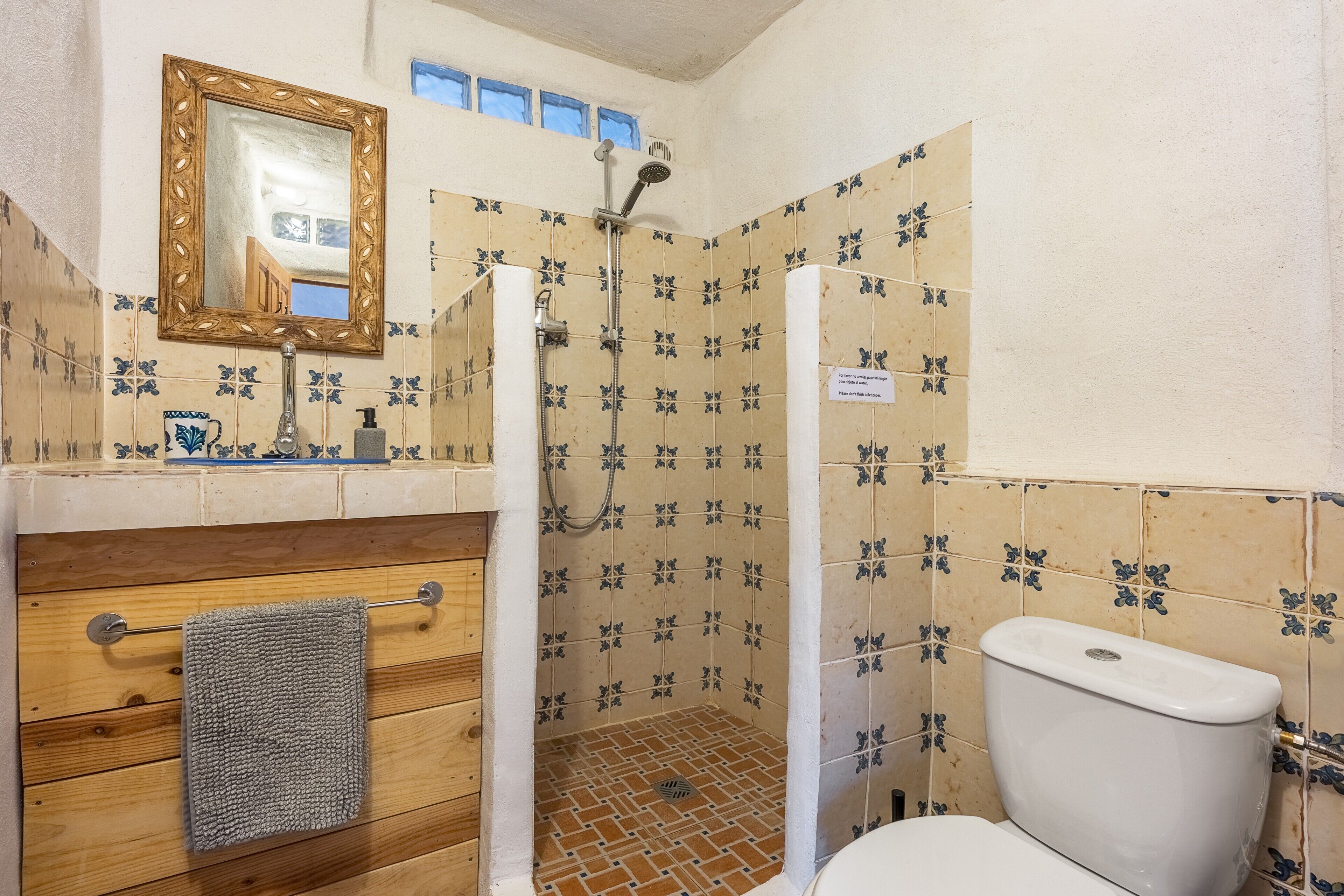Une salle de bain avec douche, toilettes, meuble-lavabo en bois et un miroir.