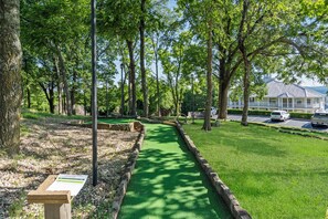 Ein Golfplatz mit einem grünen Weg, Bäumen und einem Gebäude im Hintergrund.