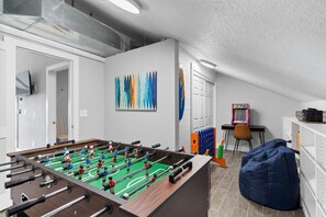 A room with a foosball table, a colorful abstract painting, a Pac-Man arcade machine, and a bean bag chair. - Newly Renovated Condo with Panoramic Lake View, Foosball, Arcade & Free Tickets Near SDC (Branson)