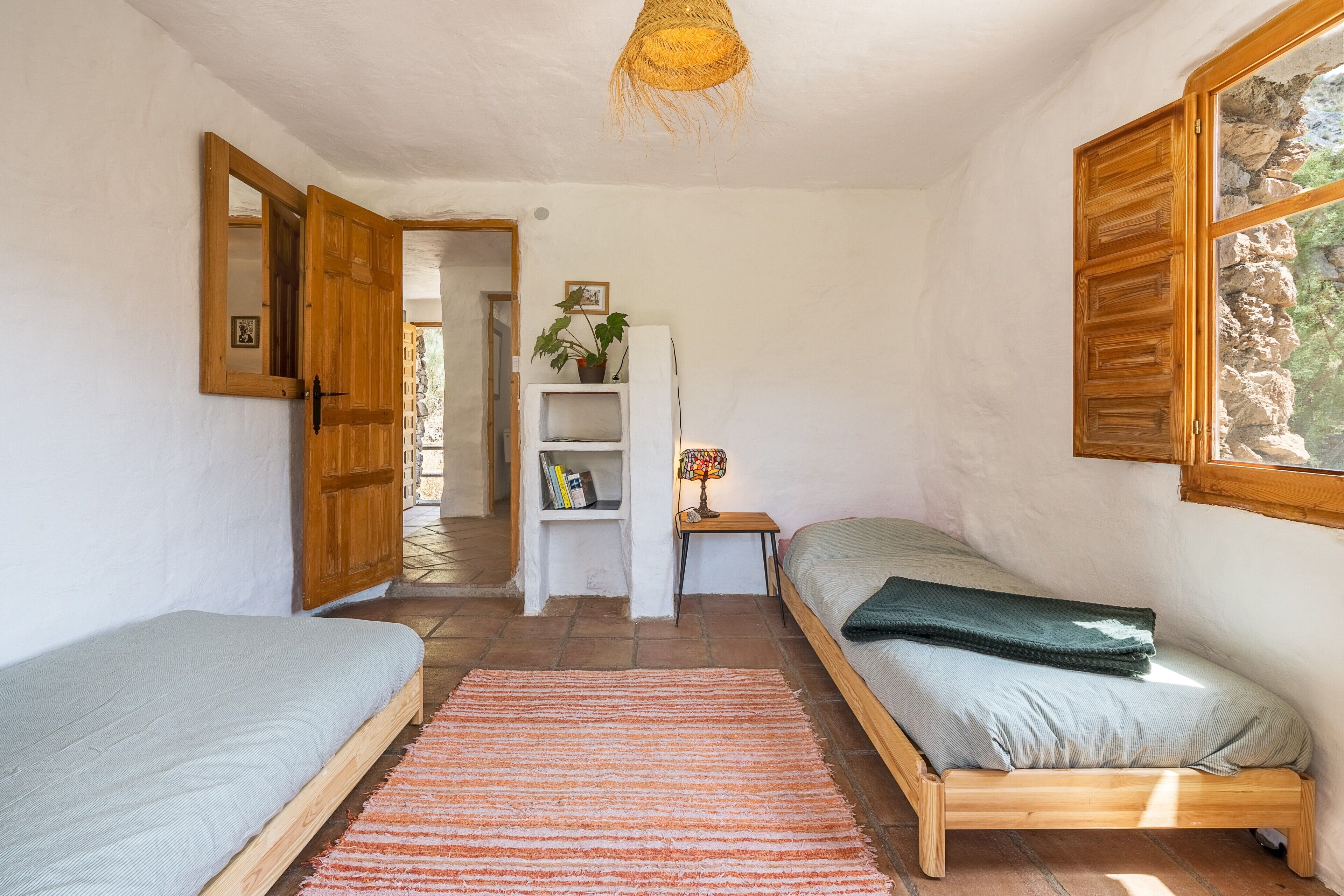 Un dormitorio con dos camas, una estantería, una lámpara y una ventana con vista a rocas.