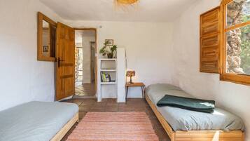Un dormitorio con dos camas, una estantería, una lámpara y una ventana con vista a rocas.