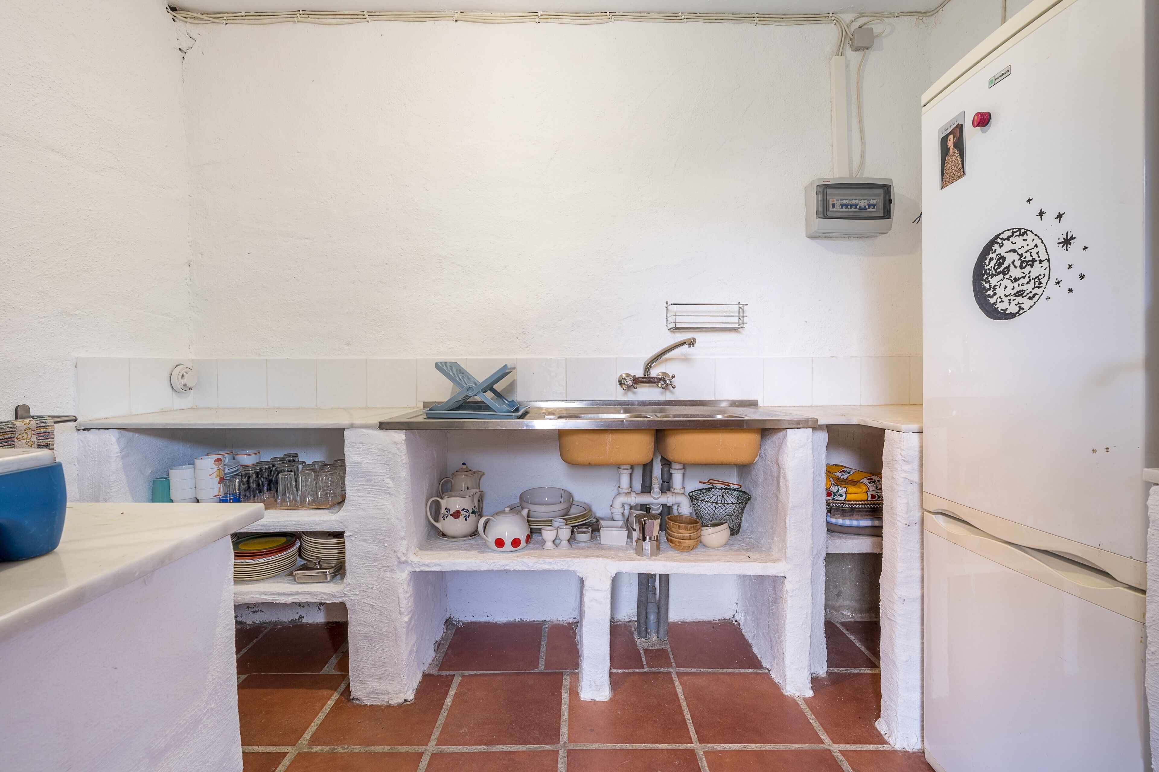 Een keuken met witte wanden, een witte gootsteen en een witte koelkast.