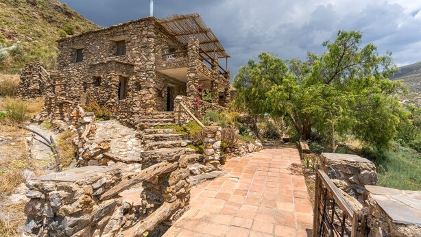 A stone building with a thatched roof, a staircase leading to the entrance, and a paved pathway.