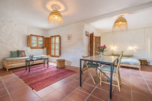 Una habitació amb taula de dinar, cadires, sofà, taula petita amb un vas, i finestra amb persianes de fusta.