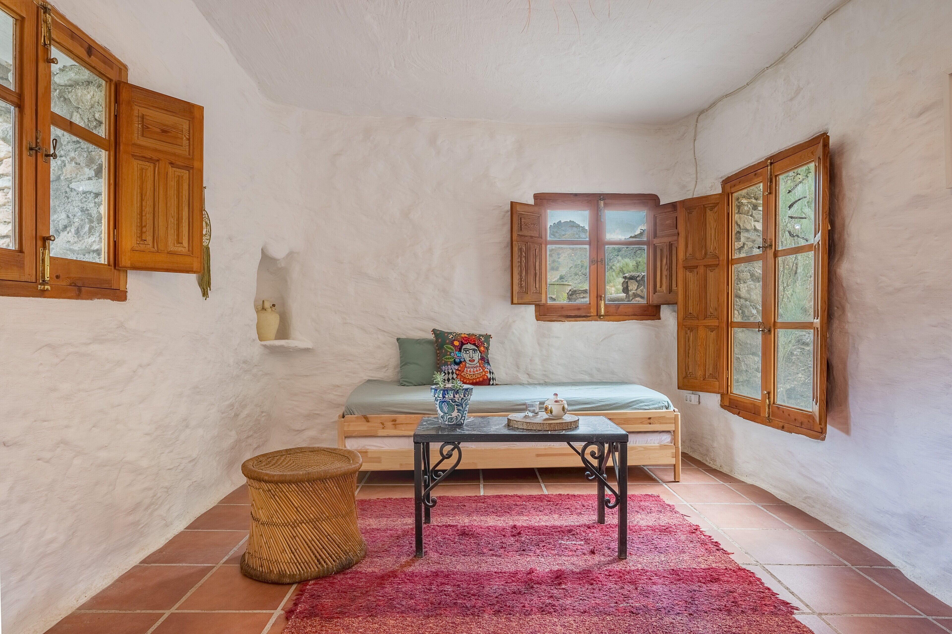 Una habitación acogedora con una cama, una mesa, una cesta de mimbre y un tapete rojo.