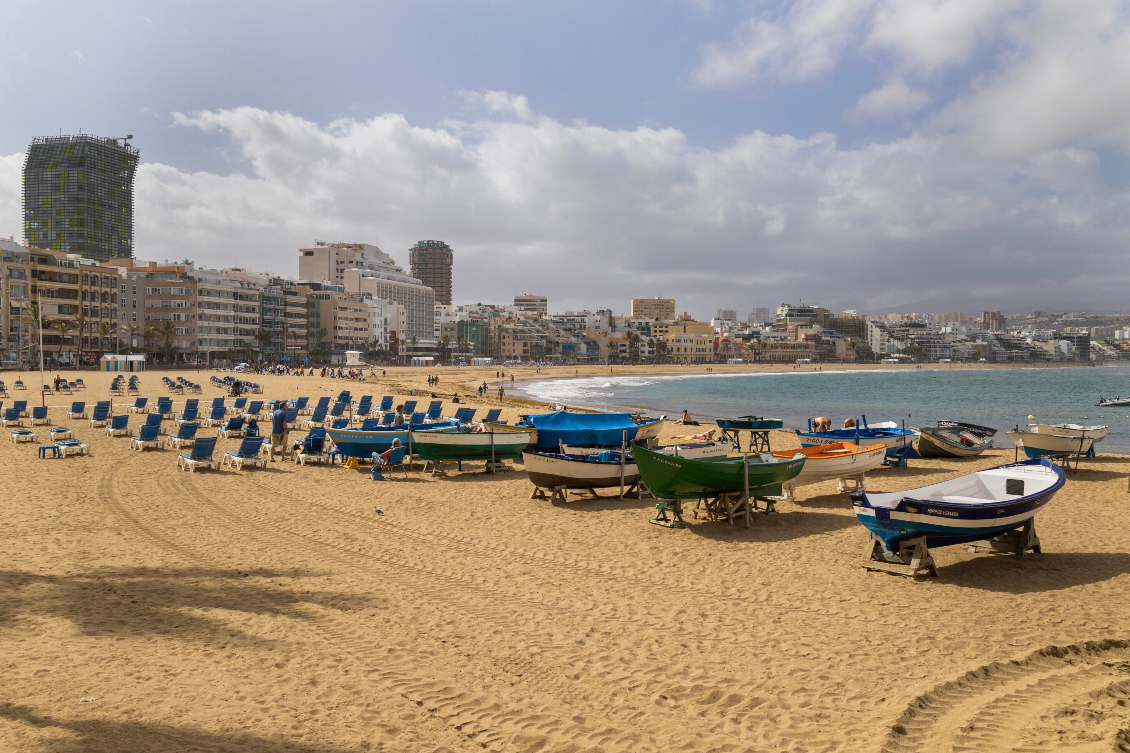 A beach with rows of sun loungers and several boats.