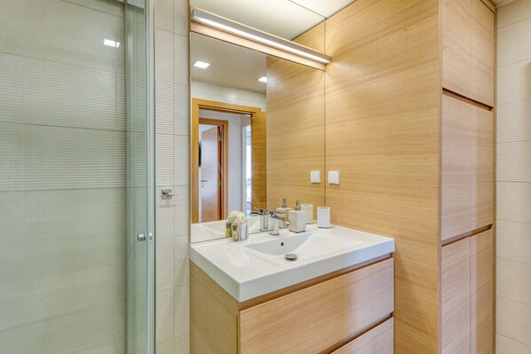 A modern bathroom with a large mirror, a white sink, and wooden cabinetry.