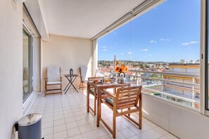 A balcony with a dining table, chairs, a trash bin, and a view of the cityscape.