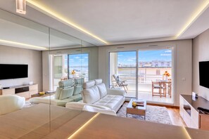 A modern living room with a sofa, a TV, and a dining area with a table and chairs.