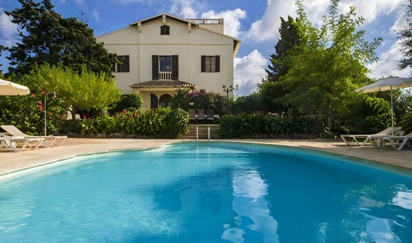 Une piscine avec des chaises longues, un bâtiment doté d’un balcon et une végétation luxuriante.