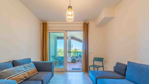 Una sala de estar moderna con dos sofás, una lámpara colgante y un ventanal corredero que da a un balcón al aire libre.