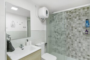 Ein modernes Badezimmer mit einer Duschkabine aus Glas, einem weißen Waschbecken und einer Toilette.