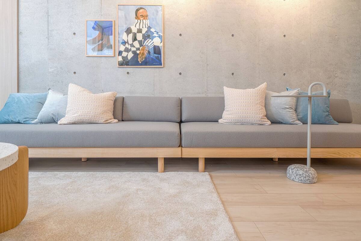 A modern living room with a grey sofa set, patterned cushions, a round wooden side table, and a floor lamp.