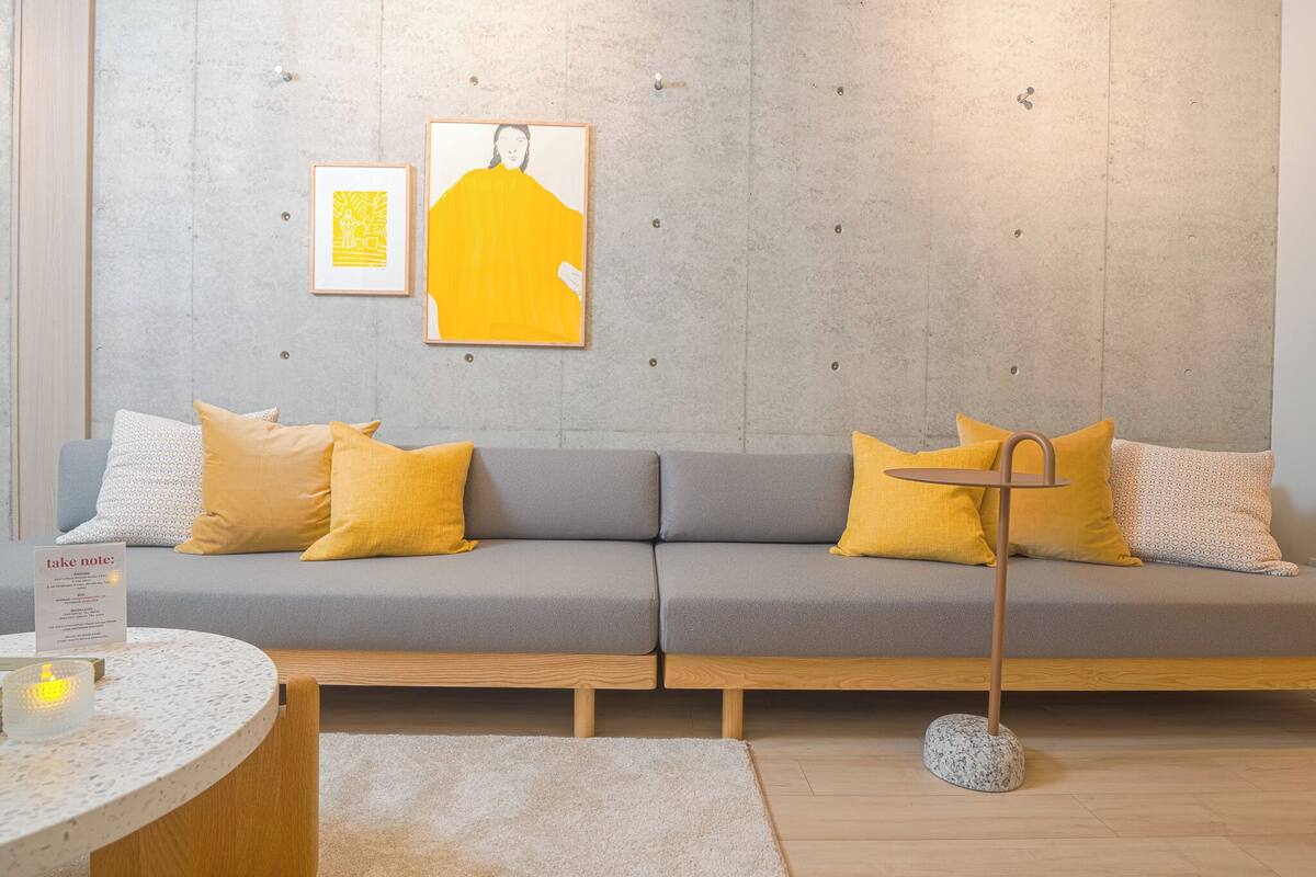 A modern living room with a grey sofa, yellow cushions, a small round table with a candle, and two framed artworks on the wall.