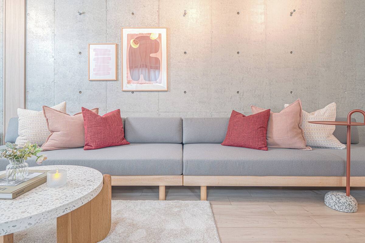 A modern living room with a grey sofa, red and white cushions, a round coffee table with a book and candle, and two framed artworks on the wall.