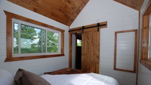 Un dormitorio con un ventanal grande, techo de madera y una cama con ropa de cama blanca y marrón.